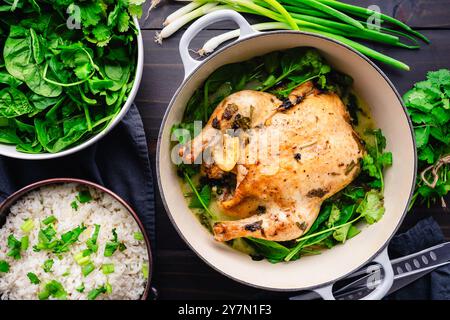 Pollo al latte di cocco con citronella in un forno olandese: Pollo arrosto circondato da spinaci e coriandolo servito con riso bianco Foto Stock