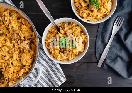 Ciotole di manzo Stroganoff guarnite con prezzemolo: Bistecca a cubetti e noodle all'uovo in salsa di panna acida ai funghi cotti in una grande teglia per brasare in ghisa Foto Stock