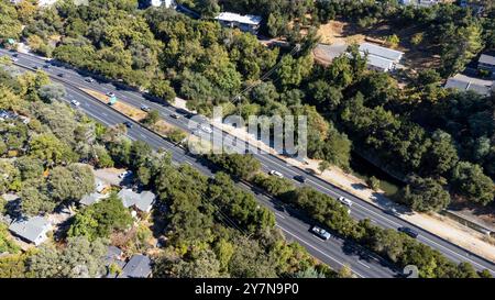 Vista aerea del traffico moderato sull'autostrada 17 a più corsie circondata da fitti alberi e case residenziali. Le linee elettriche si estendono lungo la strada, con L Foto Stock