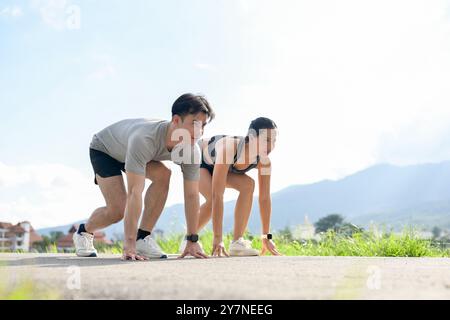 Una coppia asiatica sicura e sportiva di abbigliamento sportivo si sta preparando a fare uno sprint in una giornata di sole nel parco. competizione, maratona, corridori, stile di vita attivo Foto Stock