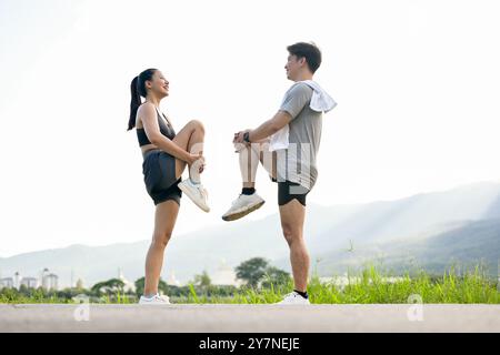 Una coppia asiatica attiva e sportiva di abbigliamento sportivo si allunga le gambe e il corpo, riscaldandosi prima di correre insieme la mattina in un parco con a S. Foto Stock