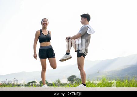 Una coppia asiatica attiva e sportiva di abbigliamento sportivo si allunga le gambe e il corpo, riscaldandosi prima di correre insieme la mattina in un parco con a S. Foto Stock