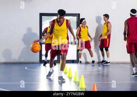 Dribbling di pallacanestro intorno ai coni, giovane atleta che pratica abilità in palestra Foto Stock