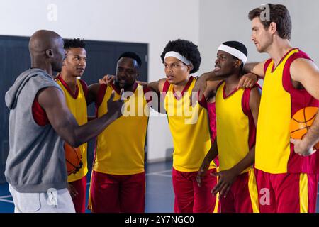 Allenatore di pallacanestro che parla con la squadra, i giocatori ascoltano e tengono in mano palle da basket Foto Stock