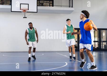 Giocando a basket, tre uomini in abbigliamento sportivo che giocano sul campo al coperto Foto Stock