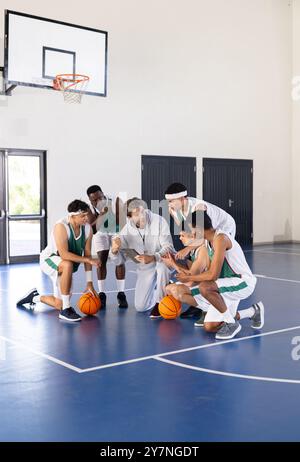 Allenatore di pallacanestro che discute della strategia con i giocatori della squadra in palestra durante le esercitazioni Foto Stock