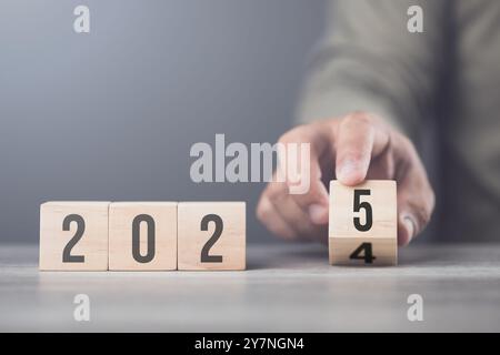 Hand sostituisce "2024" con "2025" utilizzando blocchi numerici, simboleggiando la transizione verso il nuovo anno, rappresentando il cambiamento, il progresso e i PA in corso Foto Stock