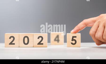 Una mano sostituisce "2024" con "2025" utilizzando blocchi numerici, simboleggiando la transizione verso il nuovo anno, rappresentando il cambiamento, il progresso e la p Foto Stock