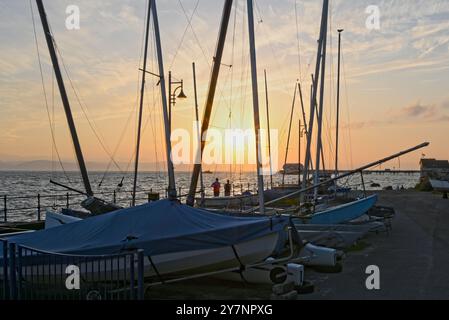 Alba a Swansea Bay da Mumbles. La luce dorata splende sul molo e i corridori che fanno jogging hanno superato le barche a vela presso la Promenade. Foto Stock