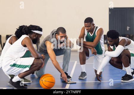 Allenatore di pallacanestro che discute la strategia con i giocatori della squadra sul campo durante le esercitazioni Foto Stock