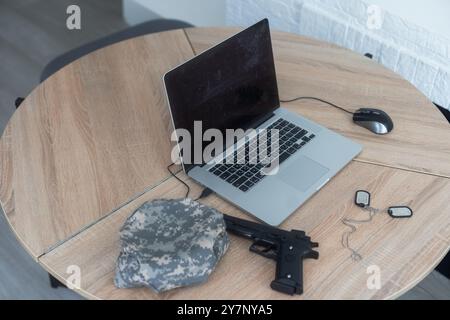 armi e computer portatile in uniforme militare sul tavolo Foto Stock