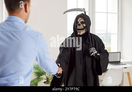 Grim Reaper con una falce sulla spalla stringe la mano a un uomo d'affari nel suo ufficio Foto Stock