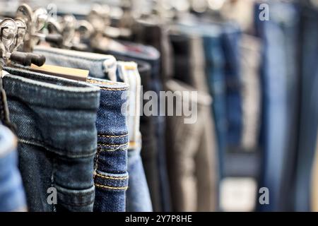 Jeans o pantaloni in denim appesi a un gancio nel centro commerciale. Collezione di articoli di moda in negozio di abbigliamento in vendita. Industria tessile. Grigio blu e b Foto Stock