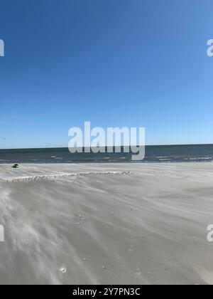 Una tranquilla spiaggia con sabbia liscia e un cielo blu limpido, caratterizzato da un oceano calmo sullo sfondo. Foto Stock