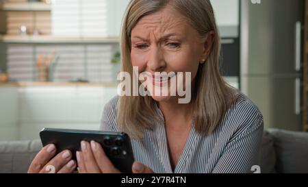 Felice felice anziano 60s matura donna caucasica anziana nonna guardare cellulare smartphone donna pensionato lettura buone notizie ricezione positivo Foto Stock