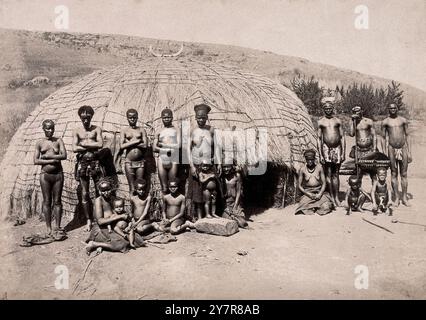 Fotografia d'epoca di nativi e kraal. Africani di fronte a una tradizionale capanna kraal. Sudafrica, tra il 1800 e il 1899. Kraal (anche scritto craal o kraul) è una parola afrikaans e olandese, usata anche nell'inglese sudafricano, per un recinto per il bestiame o altro bestiame, situato all'interno di un insediamento o villaggio dell'Africa meridionale circondato da una recinzione di rami spinosi, una palizzata, un muro di fango o altre recinzioni, grosso modo circolari. È simile a un bombardamento nell'Africa orientale o centrale. Foto Stock