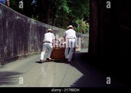 Due carreiros spingono un toboga in vimini lungo una curva ombreggiata mentre gli spettatori guardano dall'alto Foto Stock