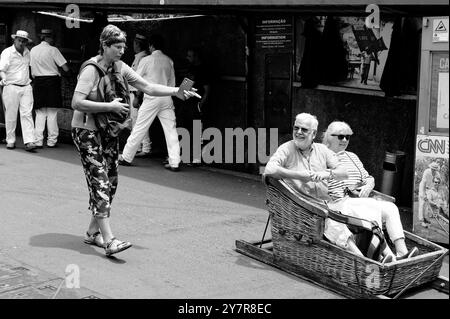 Monocromatico, che cattura i sorrisi prima del giro, i turisti maturi partono su una tradizionale slitta in vimini Foto Stock