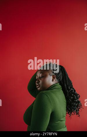 Vista laterale della bella donna africana curvata che tocca i suoi capelli intrecciati su sfondo rosso Foto Stock