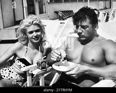 BEAUTY AND THE BEEFCAKELido Beach, New York, USA: L'attrice Jayne Mansfield sembra soddisfatta mentre accosta le sue curve in una sdraio vicino alla struttura muscolare di Mickey 'MR Universe' Hargitay al Malibu Shore Club. Si dice che il muscolo sia rimbalzato dalle sue faccende nel night club con Mae West a causa delle sue attenzioni a Miss Mansfield. Hargitay ha confermato di aver presentato all'attrice bionda un anello. Sua moglie ha presentato una causa per il divorzio a Indianapolis il 4 giugno 1956. 7 giugno 1956 Foto Stock