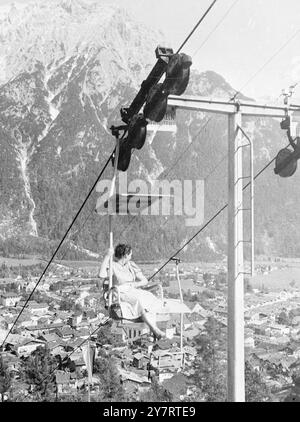 CAVALCA MITTENWALD 20.7,53. Tre anni fa, il villaggio tedesco di Mittenwald ha installato una seggiovia sulla cima di Kranzberg alta 1392 metri. Da allora, più di 300.000 passeggeri hanno goduto della vista dai 1450 metri di lunghezza. La foto mostra una splendida vista dalla seggiovia fino alla cima di 1392 metri di Kranzberg, ma la donna passeggero trova confortante tenersi al bar mentre guarda i tetti così in basso. 20 luglio 1953 Foto Stock