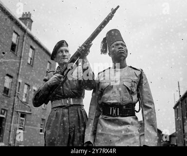 IL CONTINGENTE COLONIALE PROVA PER L'INCORONAZIONE 21.5,53. alcuni dei 500 militari e della polizia delle colonie che parteciperanno alla processione dell'incoronazione, sono in formazione a Woolwich. La foto mostra il Gunner William Thornton di Boreham Wood mostra il suo fucile al colonnello Thomas Saulo, del 4° miliardo ugandese, da Alholi, Africa 21 maggio 1953 Foto Stock