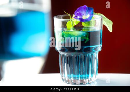 Tè di fiori viola o fiore di pisello a farfalla isolato con focalizzazione su un bicchiere su sfondo arancione Foto Stock