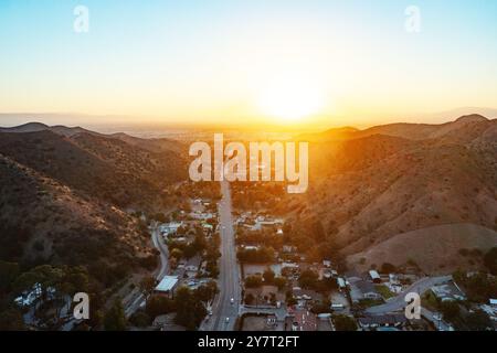 Un'ampia vista aerea che mostra una splendida città annidata tra maestose montagne mentre il sole tramonta all'orizzonte, proiettando un caldo bagliore Foto Stock