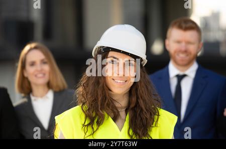 La testa di una donna arquitect manager in gilet giallo si trova di fronte al suo team aziendale che conduce un progetto importante Foto Stock