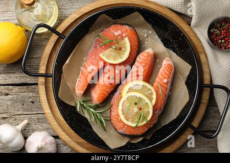 Bistecche di salmone crude fresche con spezie in padella e prodotti su tavola di legno, piatti Foto Stock