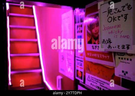 Una scala illuminata per un bar al piano superiore a Shinjuku Golden GAI con annunci pubblicitari presso l'entrata. In questa zona di Shinjuku, Tokyo, Giappone, ci sono oltre 200 piccoli bar in stile baraccopoli, club e ristoranti Foto Stock