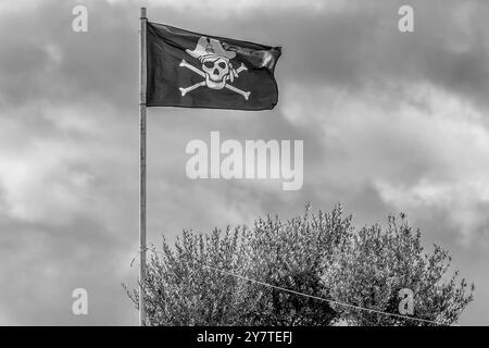 Una divertente bandiera dei pirati contro il cielo nuvoloso in bianco e nero Foto Stock