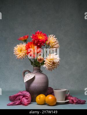 Brillanti fiori autunnali. Bouquet lussureggiante di dalie di diversi colori in grande vaso. Accanto a due prugne gialle, tazza. La natura morta crea un'atmosfera di Foto Stock