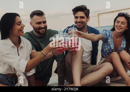 Gruppo di giovani allegri che brindano con cocktail mentre trascorrono del tempo in spiaggia insieme Foto Stock