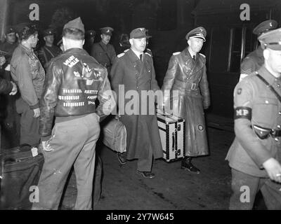 GENERALI TEDESCHI A LONDRA foto mostra: Il maggiore generale Muller (a sinistra) e il maggiore generale Maier, dell'esercito tedesco, passano uno degli uomini che hanno portato la sconfitta nel Reich, mentre si preparano a salire a bordo di un treno alla stazione di Euston, Londra. È sergente tecnico J B Alexander, del Rhode Island, New York, operatore radio del bombardiere Weary Willie. Le bombe dipinte sulla sua giacca volante mostrano il numero delle sue missioni. 17 maggio 1945 Foto Stock