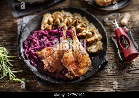 Porzione di anatra arrosto gamba cavolo rosso gnocchi fatti in casa sulla piastra e vino rosso sullo sfondo. Foto Stock