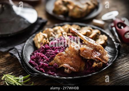 Porzione di anatra arrosto gamba cavolo rosso gnocchi fatti in casa sulla piastra e vino rosso sullo sfondo. Foto Stock