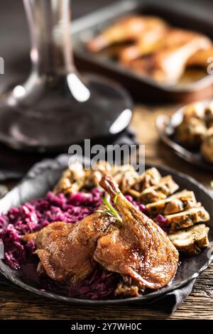 Porzione di anatra arrosto gamba cavolo rosso gnocchi fatti in casa sulla piastra e vino rosso sullo sfondo. Foto Stock