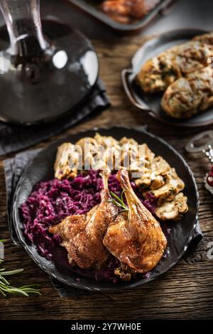 Porzione di anatra arrosto gamba cavolo rosso gnocchi fatti in casa sulla piastra e vino rosso sullo sfondo. Foto Stock