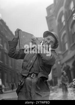 Un tipico membro dell'Auxiliary Military Pioneer Corps che si schiera allegramente con un pezzo di muratura caduta mentre aiuta a rimuovere i detriti dopo un raid aereo a Londra. 1940 Foto Stock