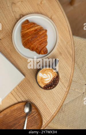 Un tavolo in una caffetteria, con una tazza di cappuccino, deliziosi pasticcini e riviste. Vista dall'alto. Foto Stock