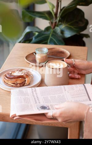Le mani di una donna tengono una tazza di caffè mentre leggono il giornale in un bar. Vista laterale. Foto Stock