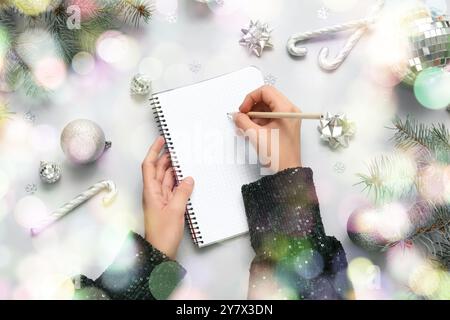 Donna che scrive piani per il nuovo anno con notebook e decorazioni natalizie su sfondo chiaro Foto Stock