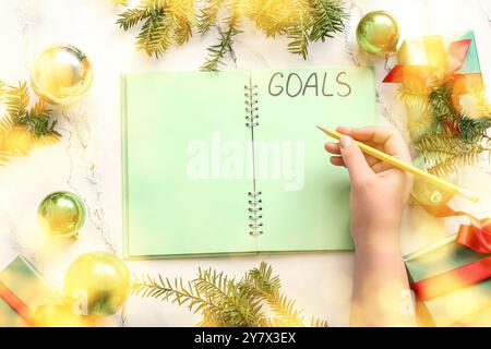 Donna che scrive OBIETTIVI DI testo su notebook e decorazioni natalizie su sfondo chiaro Foto Stock