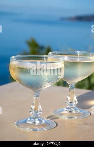 Spumante freddo, cava o champagne in due bicchieri da coupé sul tavolo con vista sul mare blu vicino a Mentone e Monte Carlo, Costa Azzurra, la Francia è estate Foto Stock