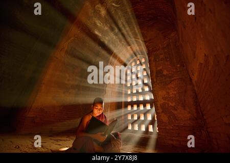 Un giovane monaco di lettura con raggi di sole e in templi di Bagan, Myanmar. Foto Stock