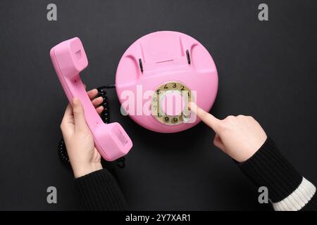 Mani femminili con telefono retrò rosa su sfondo nero Foto Stock