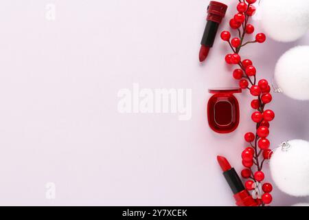 Bellissima composizione con palline bianche di Natale, contenitore con rossetto e ramo di bacche rosse su sfondo rosa pallido Foto Stock