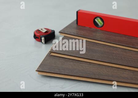 Metro a nastro, livella e pezzi per pavimenti in laminato su superficie ruvida grigia, primo piano Foto Stock