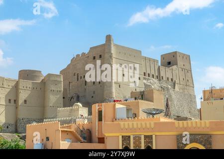 Fortezza della cittadella di Bahla mura in pietra e torri rotonde con edificio residente e in primo piano, Bahla, Oman Foto Stock